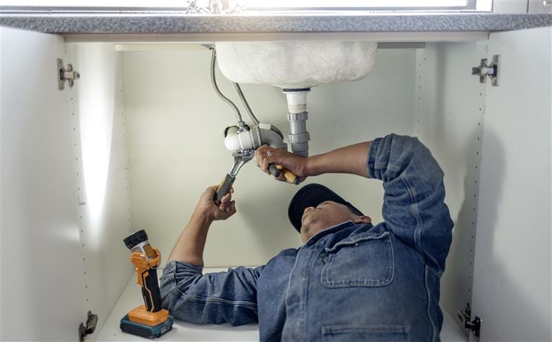 Plumber repairing pipes beneath a bathroom sink in Menifee