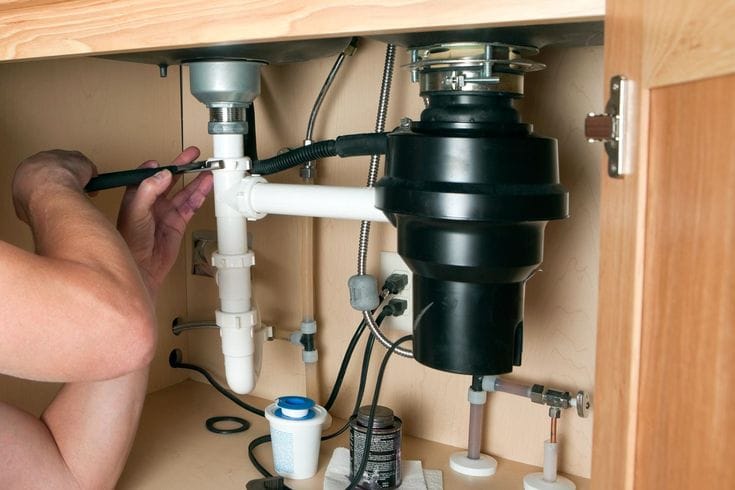Plumber installing a garbage disposal beneath a kitchen sink in Menifee