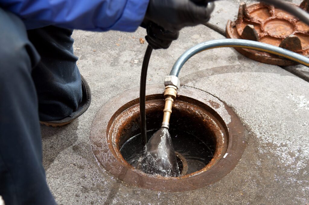 Plumber hydro jetting a sewer line through a manhole in Menifee