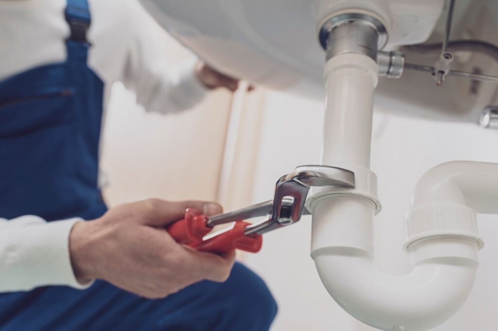 Plumber repairing a white drain pipe beneath a sink in Menifee