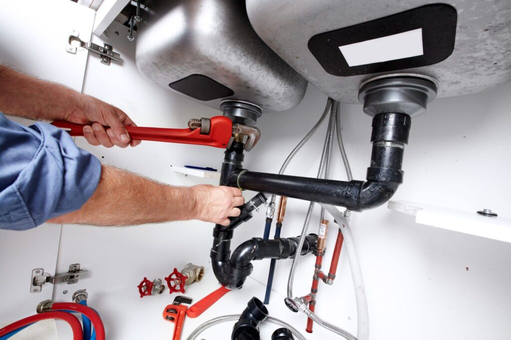 Plumber repairing drain pipes beneath a kitchen sink in Menifee
