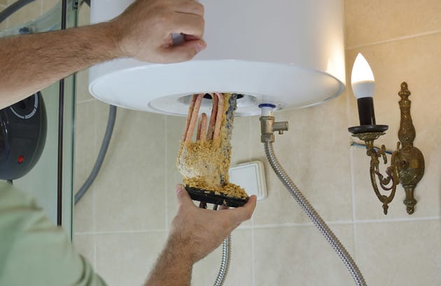 Technician removing mineral buildup from a water heater in Menifee